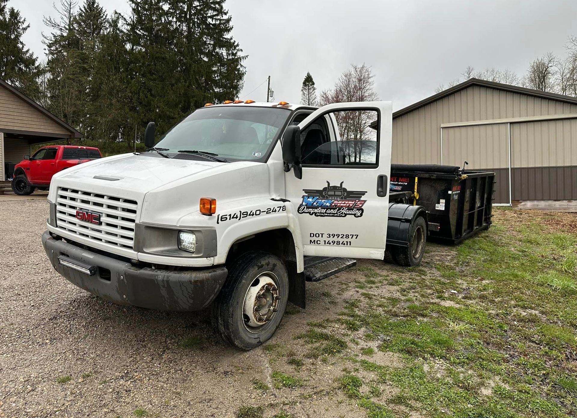 A white dump truck is parked in a gravel lot next to a building.