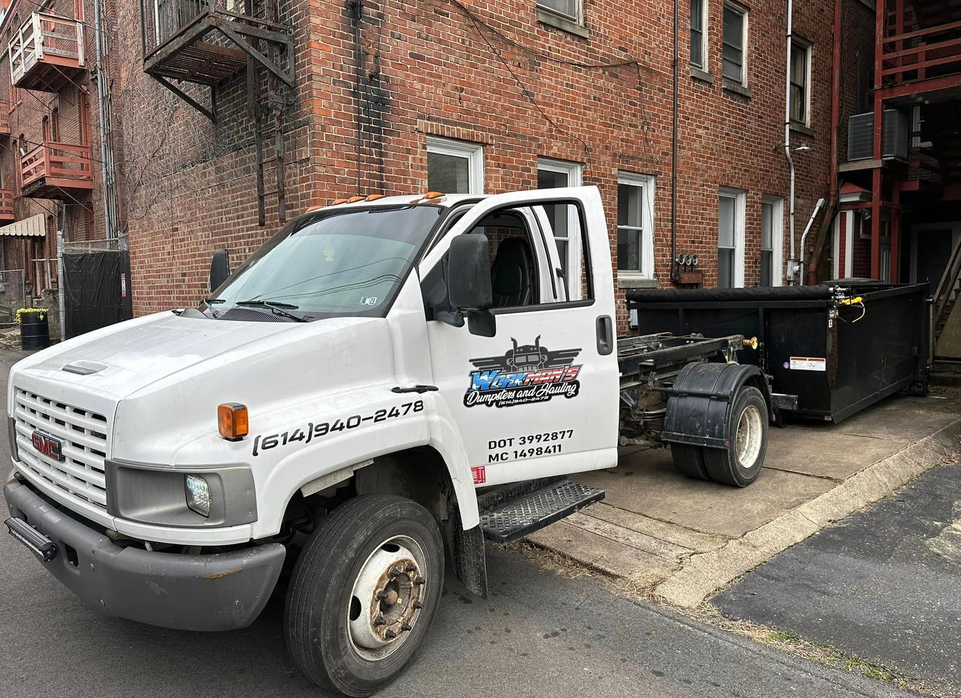 A white dump truck is parked in front of a brick building.