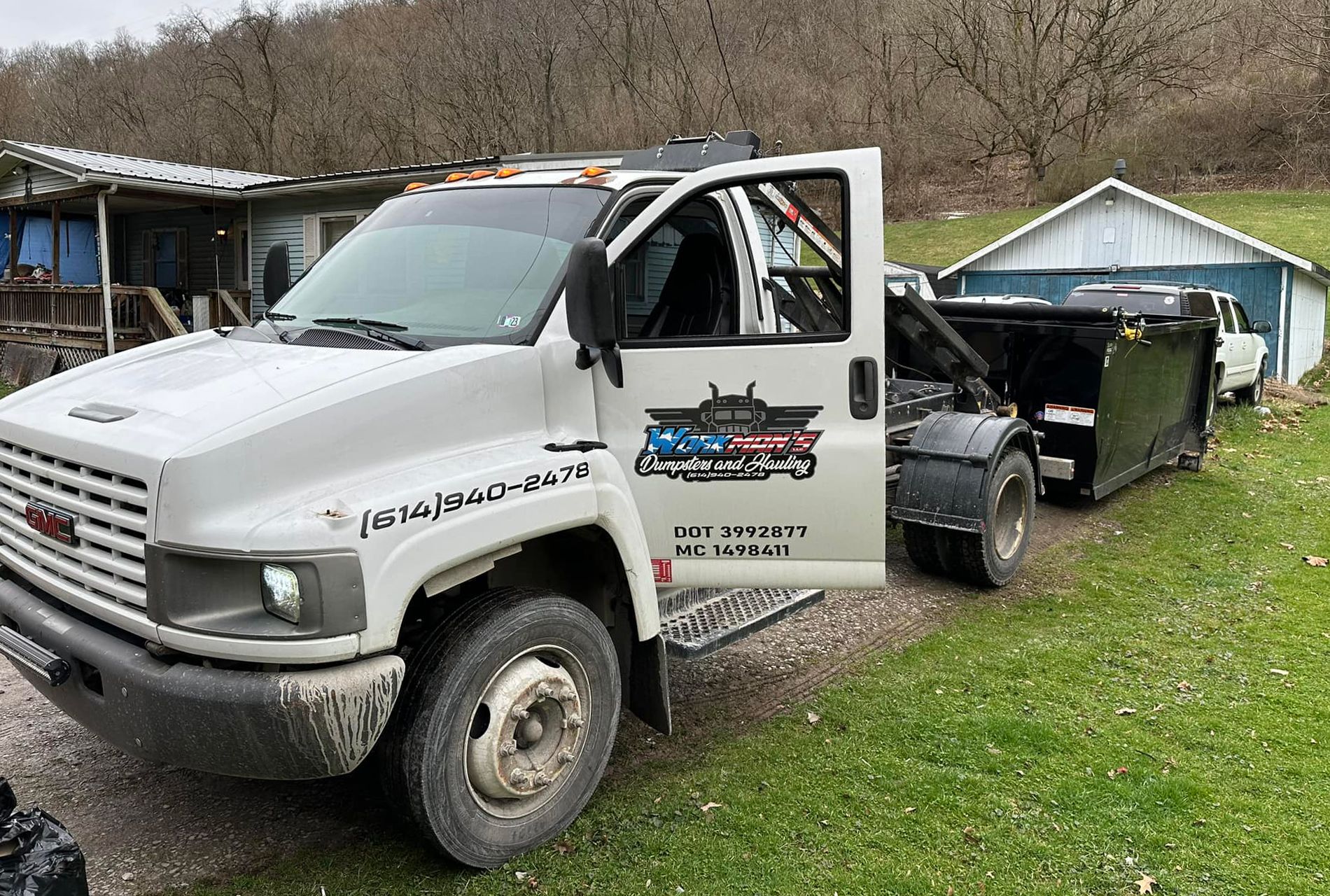 A white tow truck is parked in a grassy field next to a house.