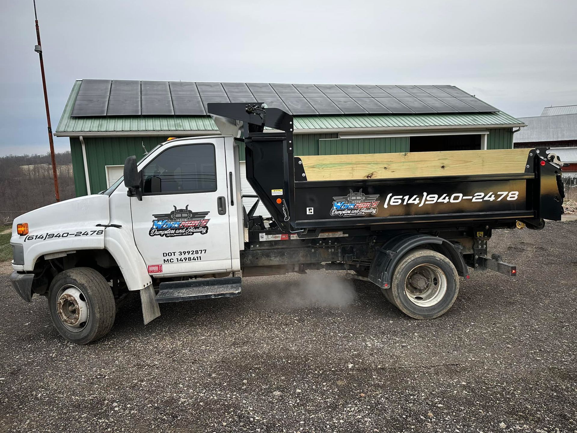 A dump truck is parked in front of a building with solar panels on the roof.