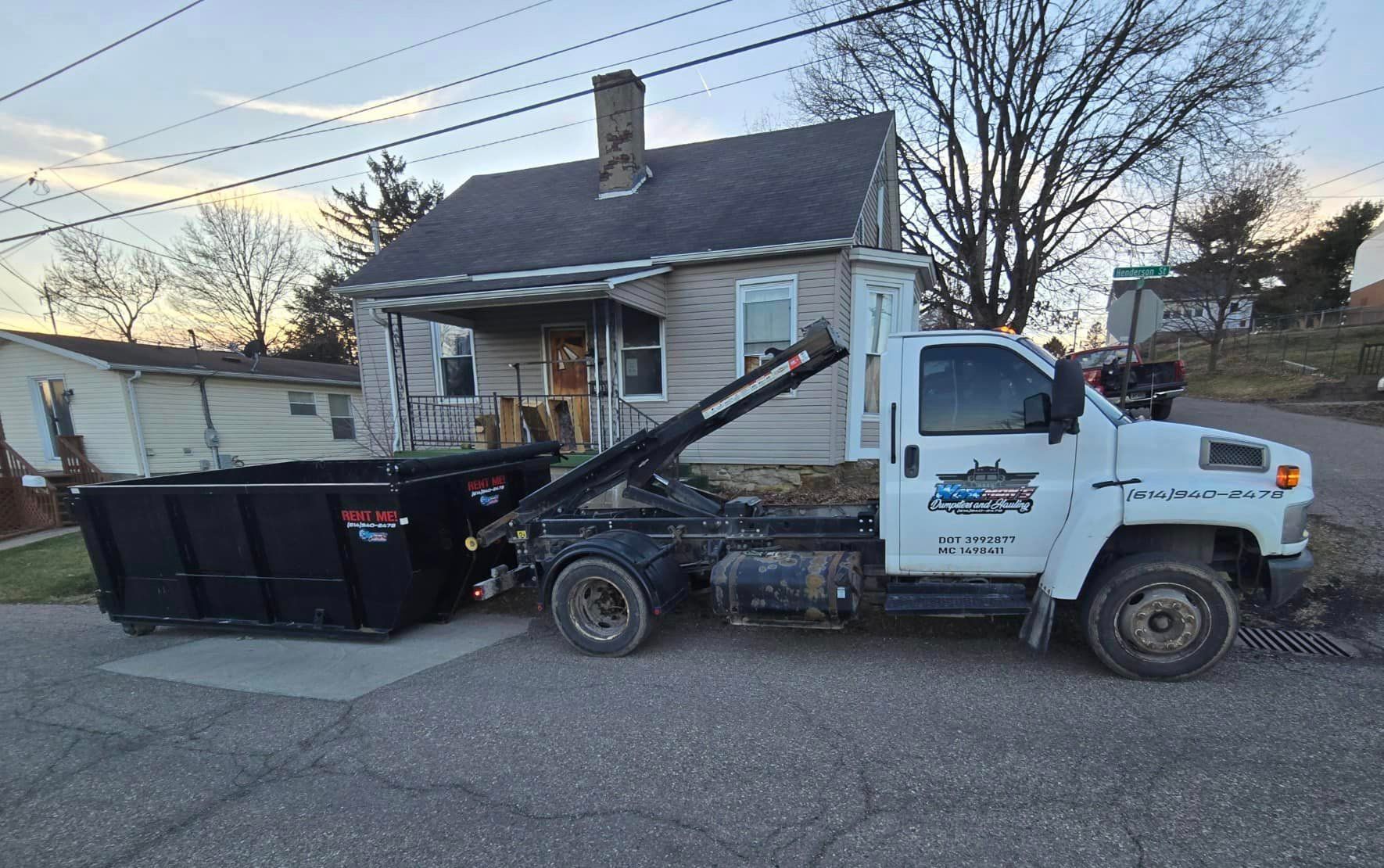 A dumpster truck is parked in front of a house.