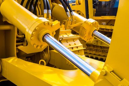Yellow hydraulic machinery with polished metal pistons in an industrial setting