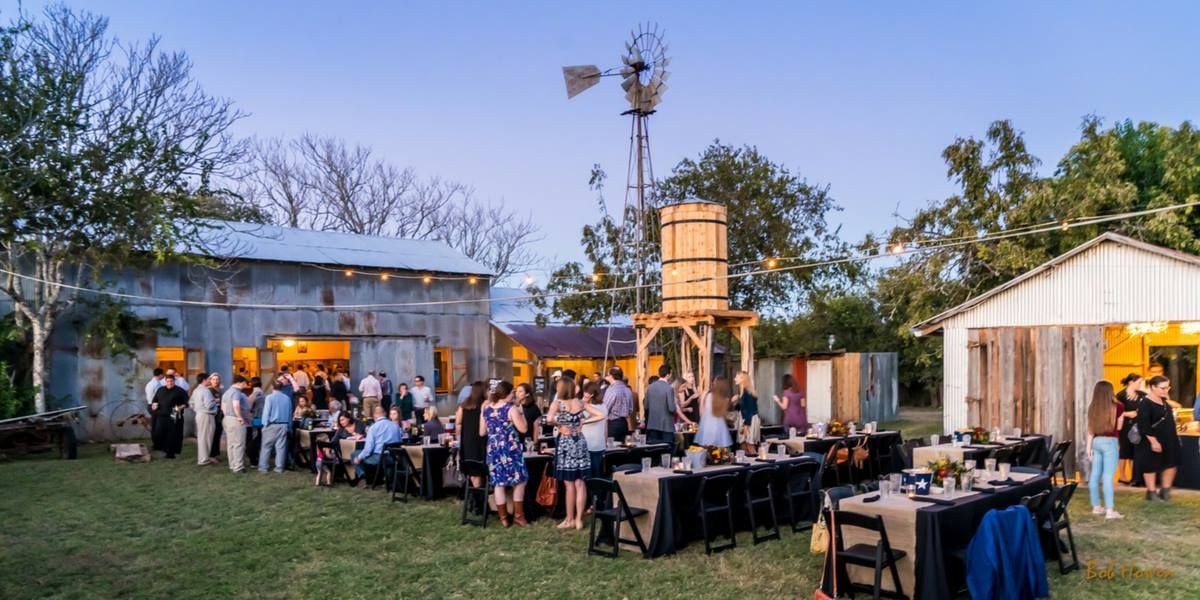 A group of people are sitting at tables in a field with a windmill in the background.