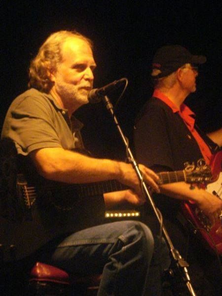 A man sings into a microphone while another man plays a guitar.