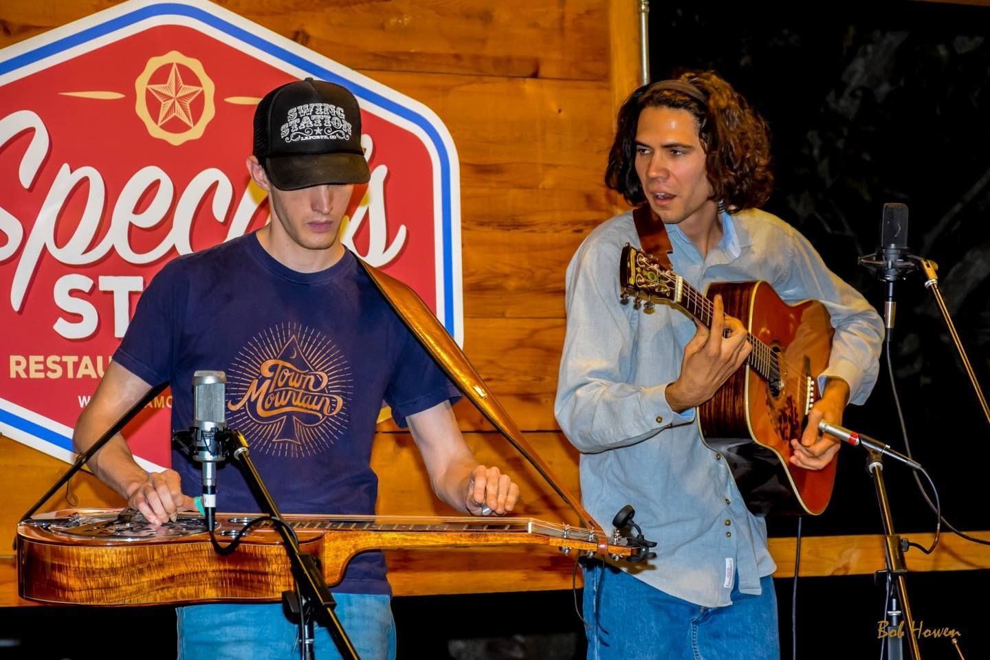Two men are playing guitars in front of a sign that says specs.