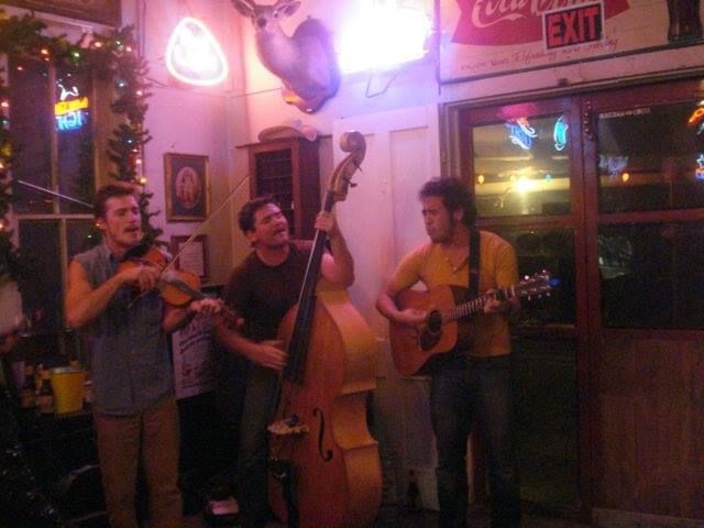 Three men are playing instruments in front of a Coca-Cola sign.
