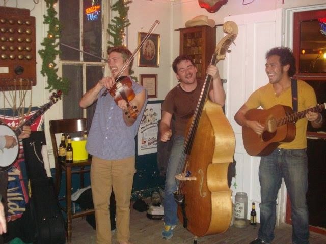 A man playing a violin and two men playing guitars in a room.
