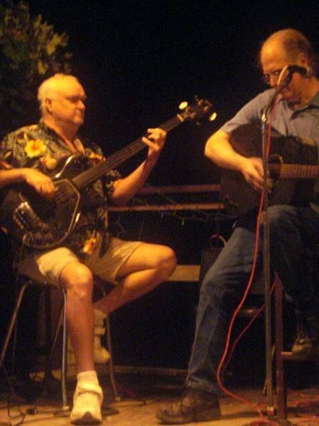 Two men are playing guitars and singing into microphones on a stage.
