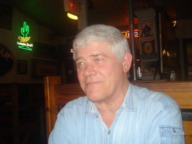 A man in a blue shirt is sitting at a table in a restaurant.