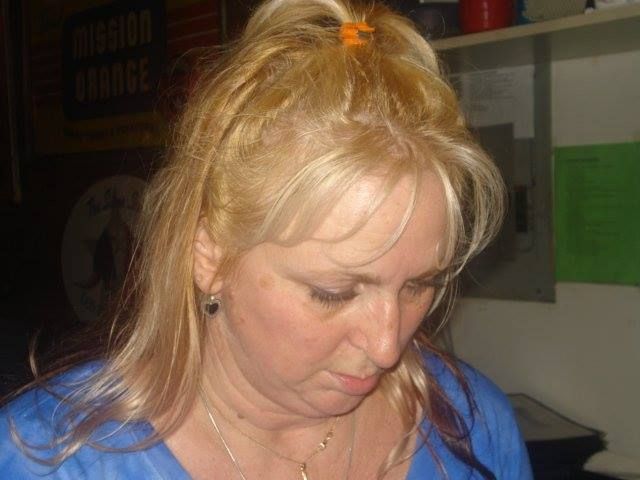 A woman with blonde hair is wearing a blue shirt and earrings.