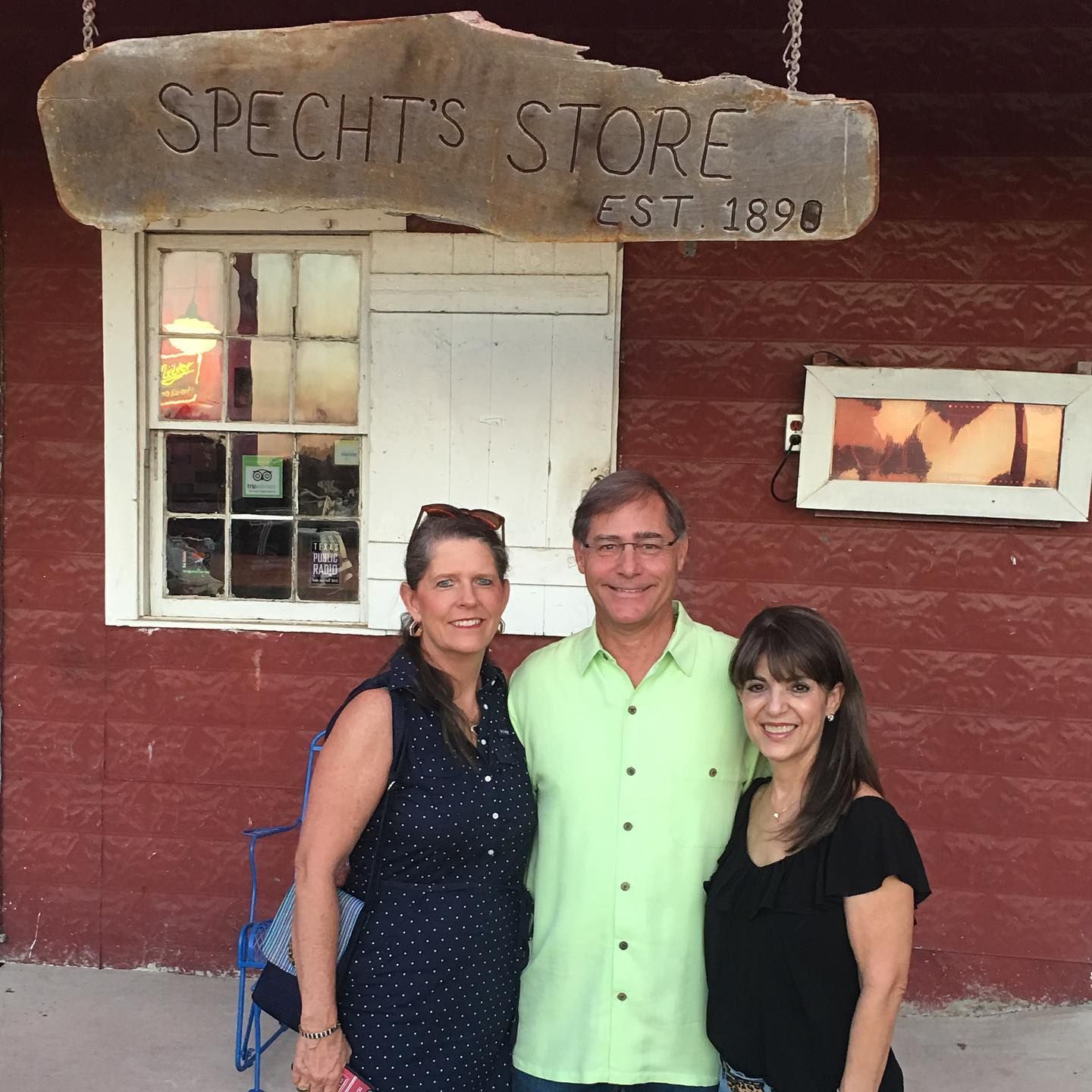 Three people are posing for a picture in front of a store called Specht's store.