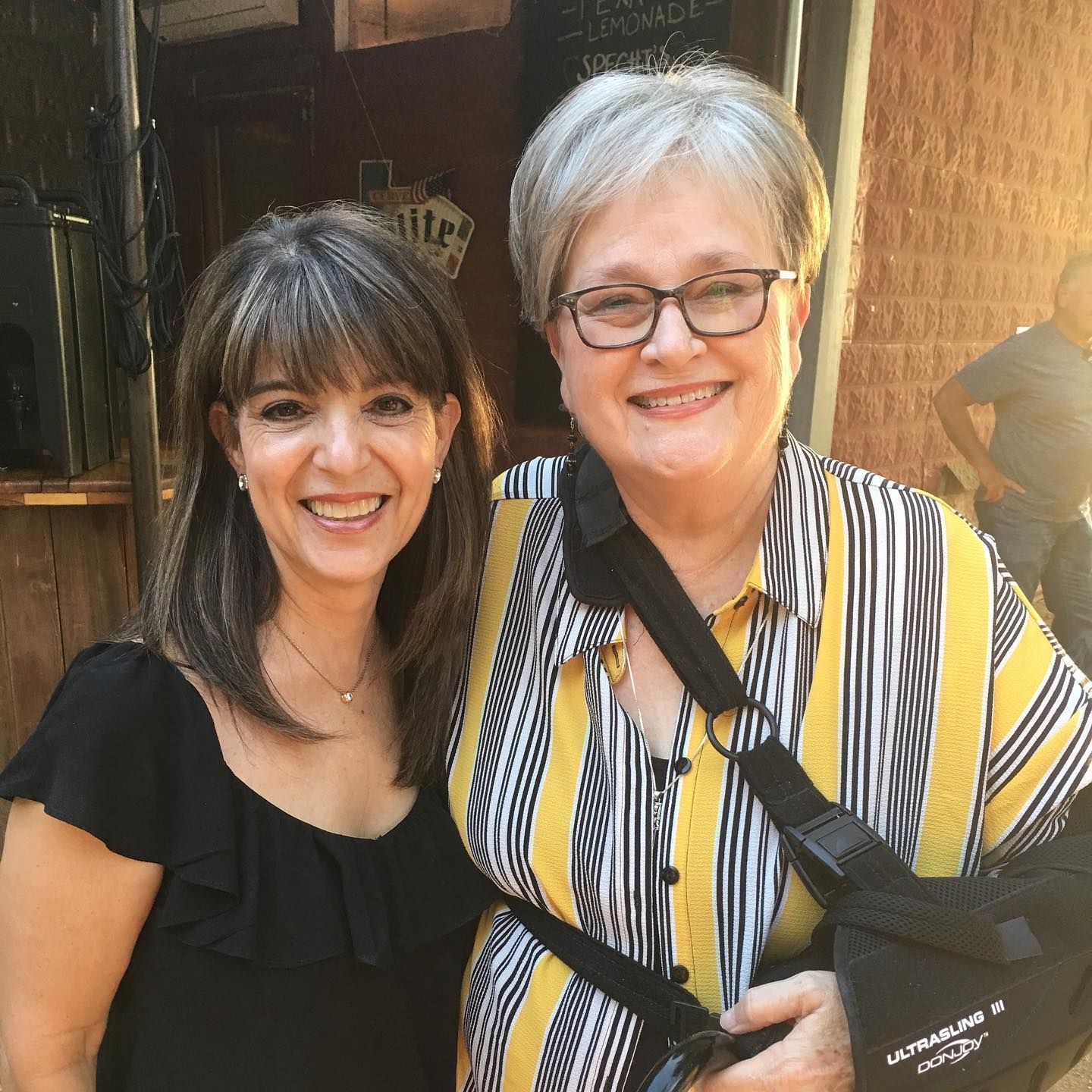 Two women are posing for a picture and one has a broken arm.