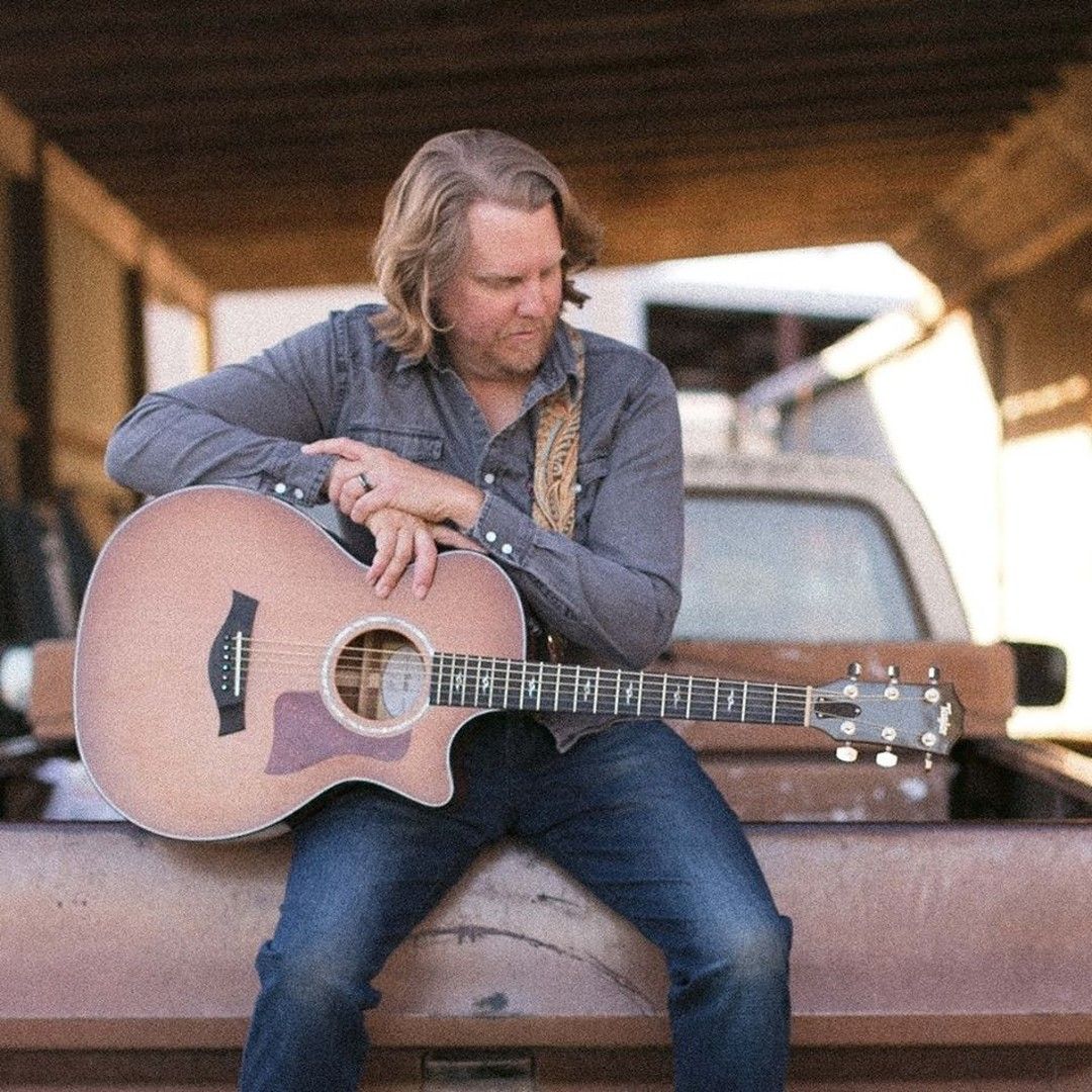 A man is sitting on the back of a truck holding a guitar.