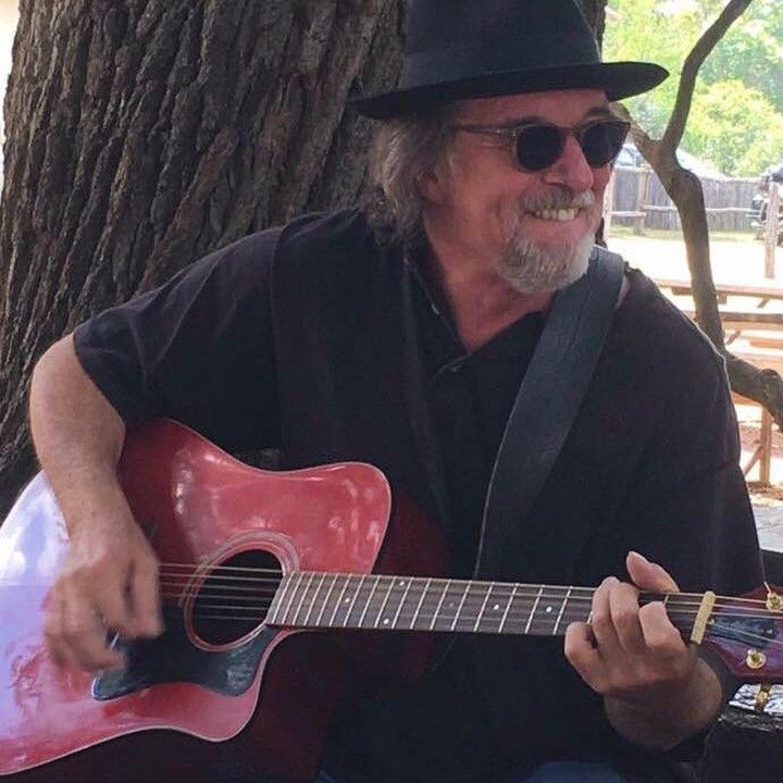 A man wearing a hat and sunglasses is playing a red guitar.