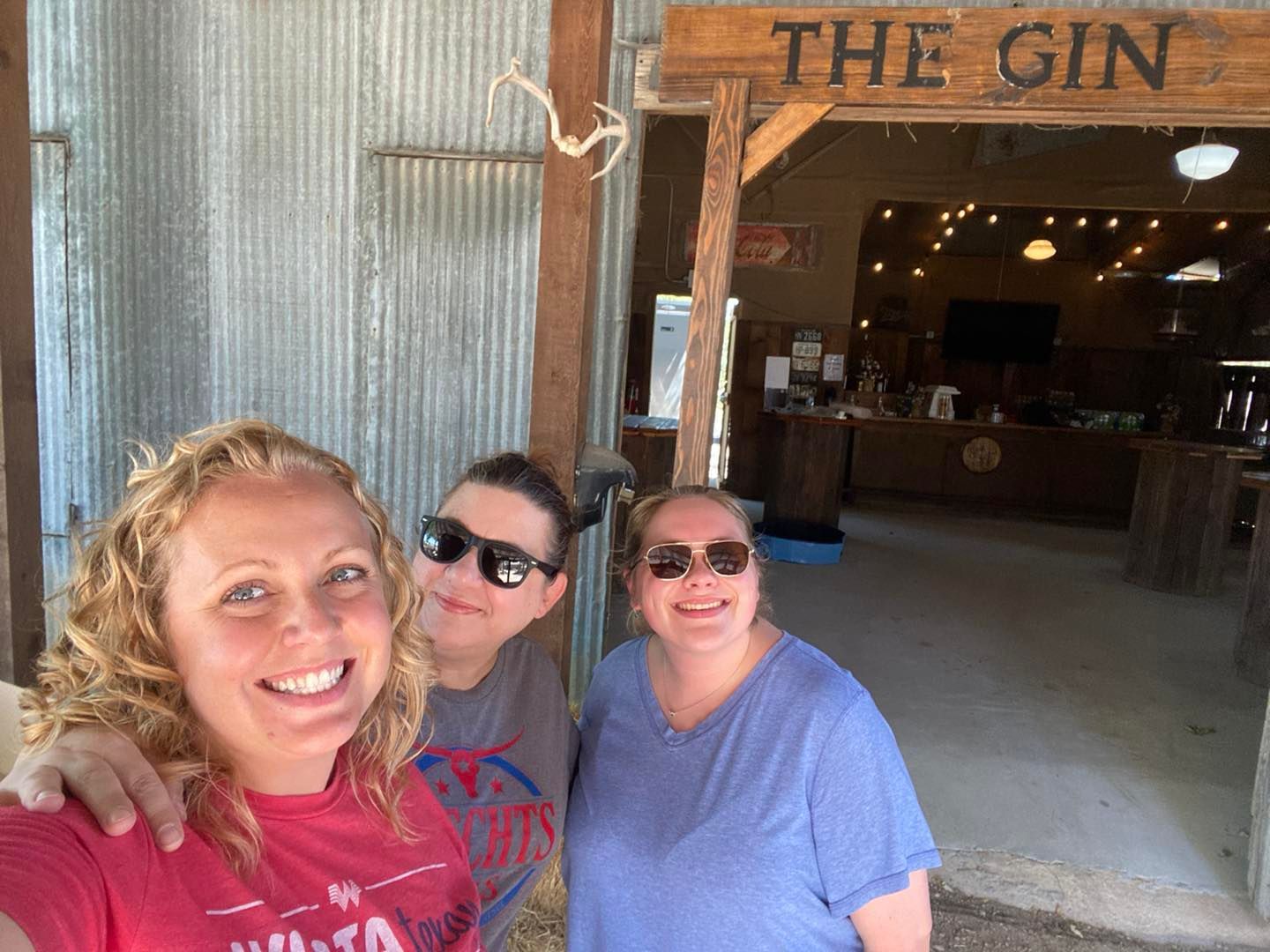 Three women are posing for a picture in front of a sign that says the gin.