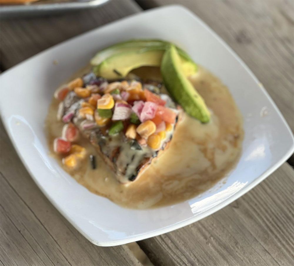 A white plate topped with a slice of pizza and avocado.
