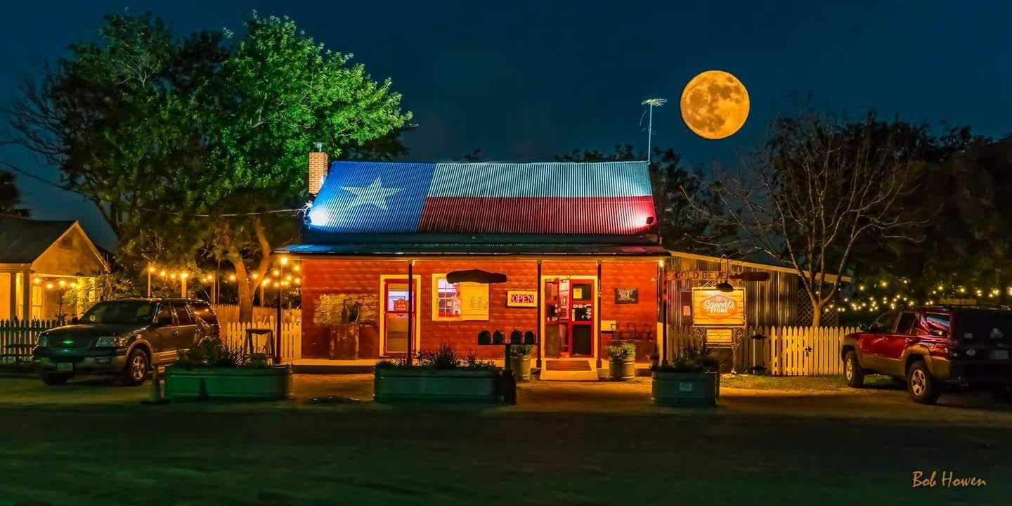 A restaurant with a Texas flag on the roof at night with a full moon in the background.
