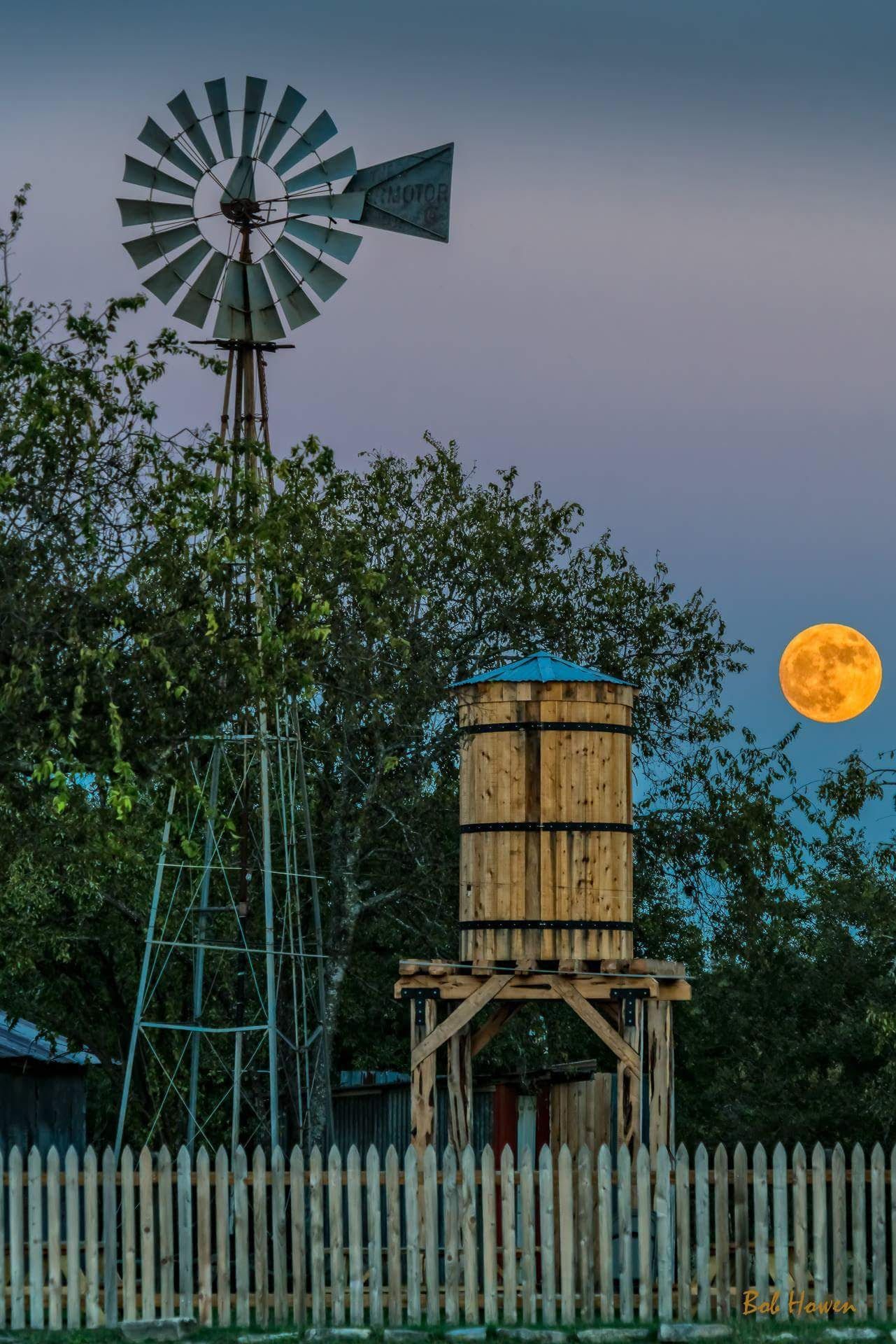 A windmill and a water tower with a full moon in the background.