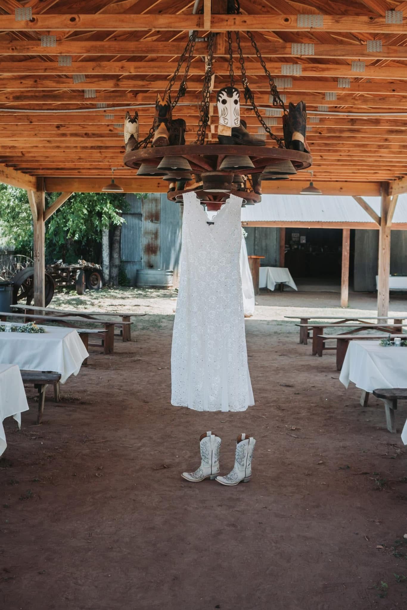 A bride's wedding dress and cowboy boots are hanging from a chandelier.