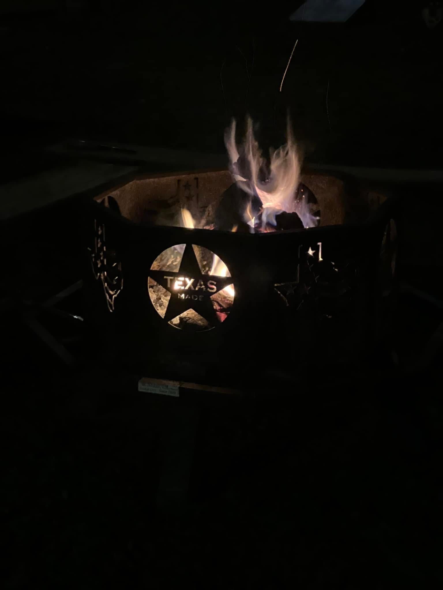 A fire pit with a Texas star on it is lit up at night.