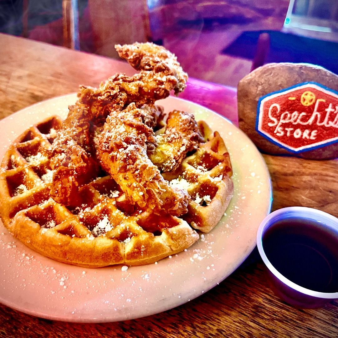 A plate of chicken and waffles next to a cup of syrup.