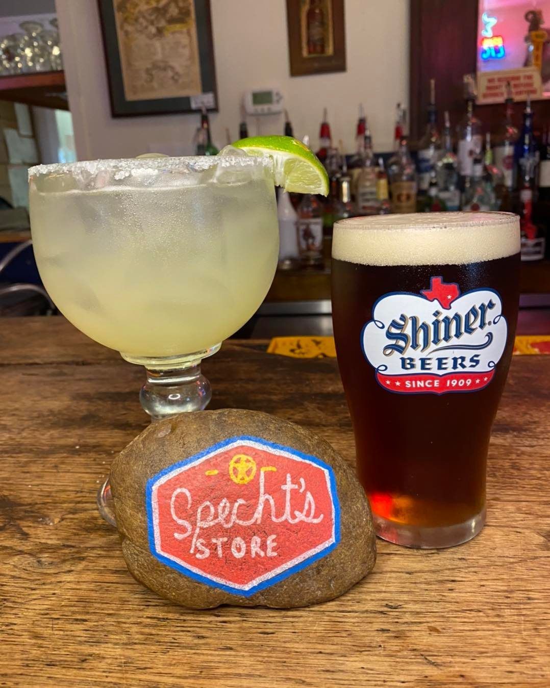 A margarita and a glass of shiner beer are on a bar.