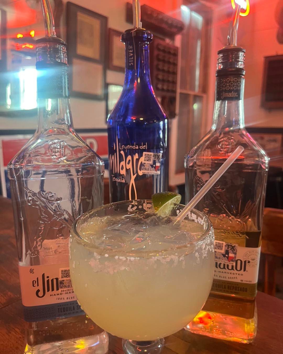 A margarita is sitting on a table next to two bottles of tequila.