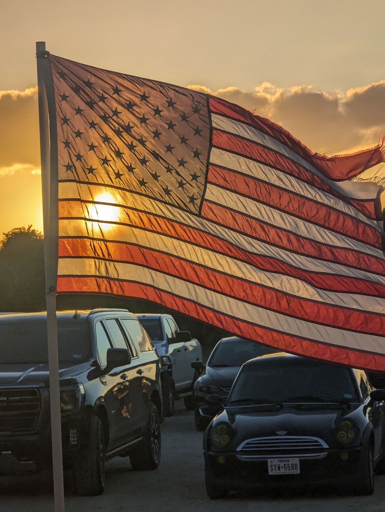 A large American flag is flying over a parking lot.