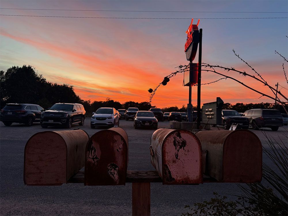 A row of mailboxes in a parking lot at sunset.