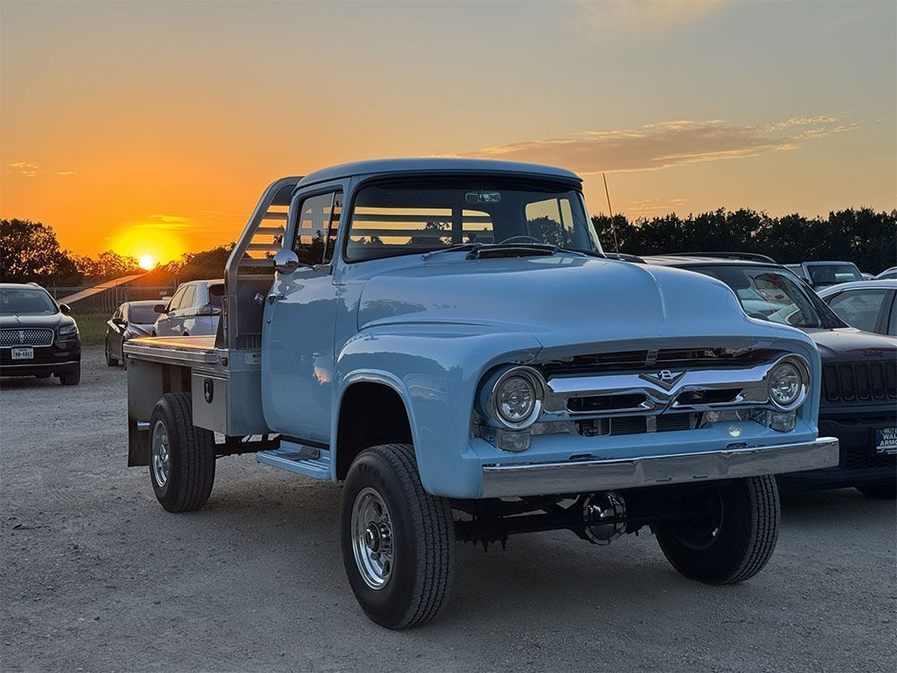 A blue truck is parked in a parking lot at sunset.