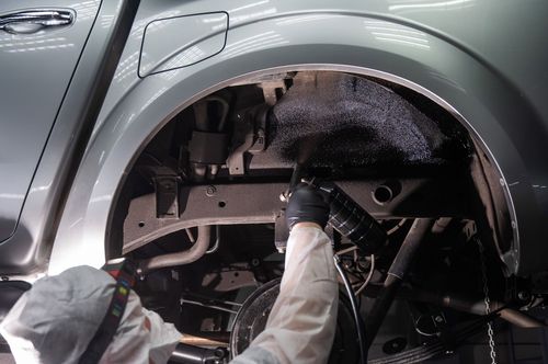 Mechanic inspecting the inside of a car wheel well with a flashlight during repair