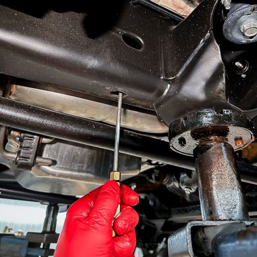 Red-gloved hand using a screwdriver on the underside of a vehicle near a suspension joint