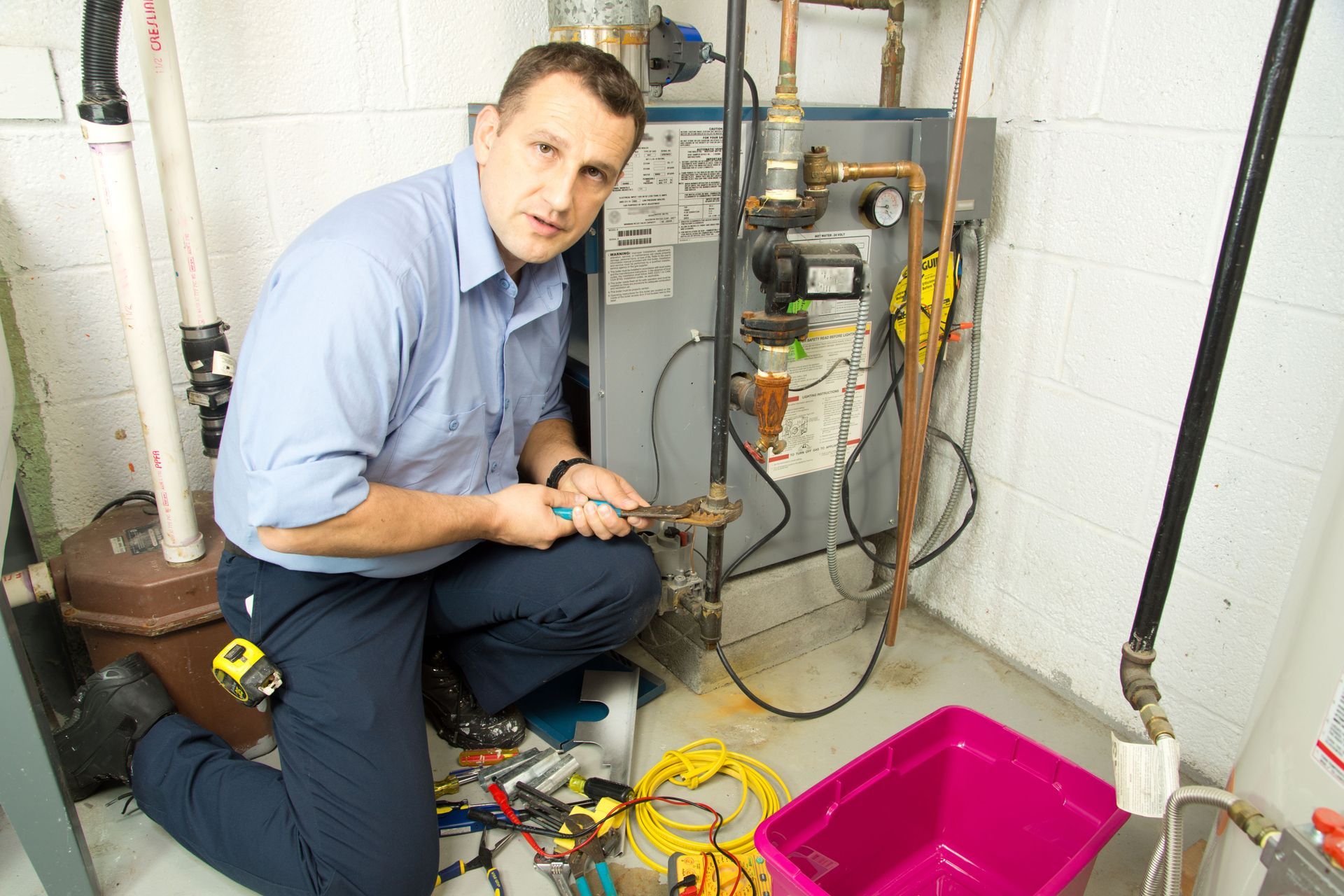 Technician inspecting a boiler in a utility room, with tools and a pink basin nearby