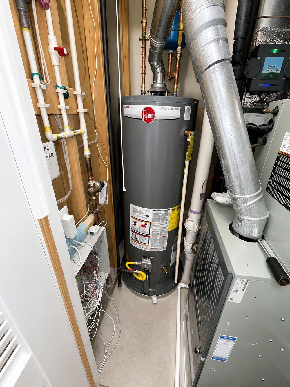 Tall gray water heater in a cramped utility closet with exposed pipes and ducting.