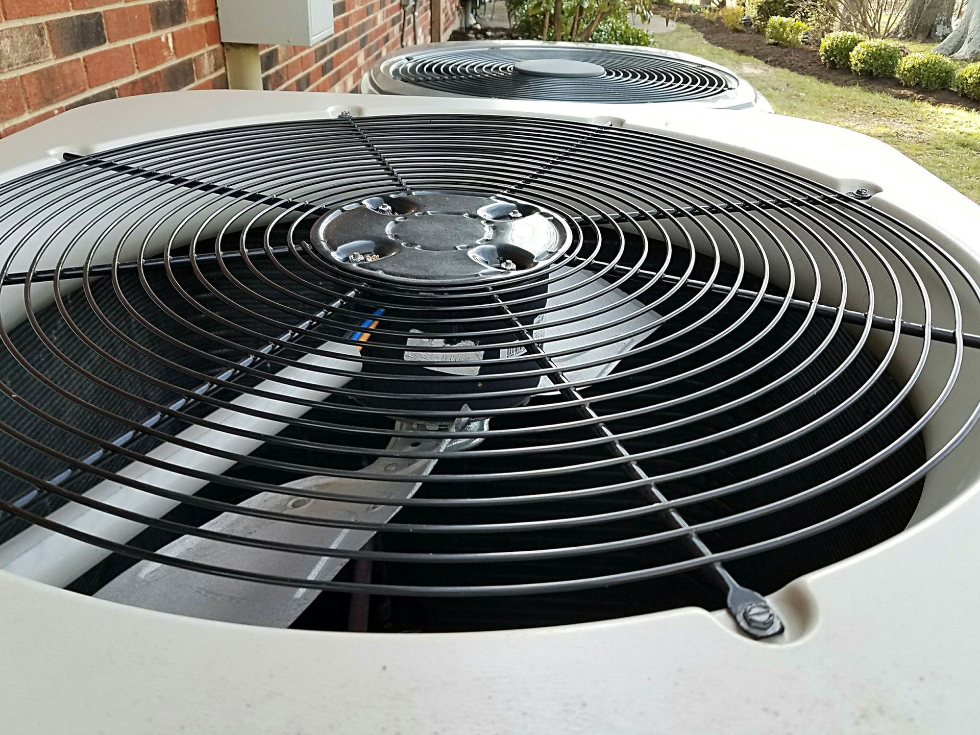 Close-up of two outdoor air conditioner units with black fan grilles beside a brick wall.