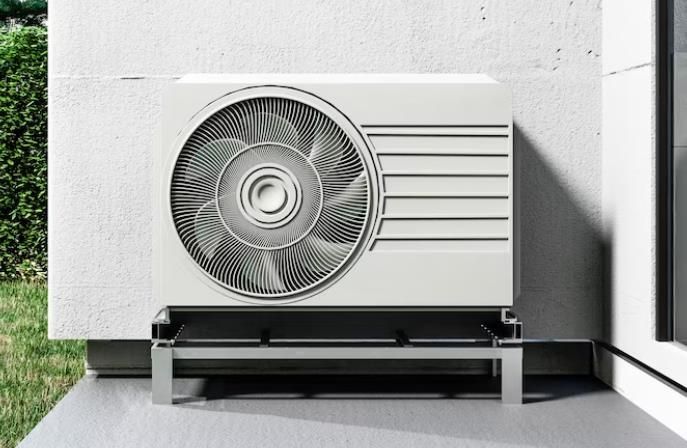 Outdoor air conditioning unit beside a wall on a concrete patio, with a fan grille and vented side panel