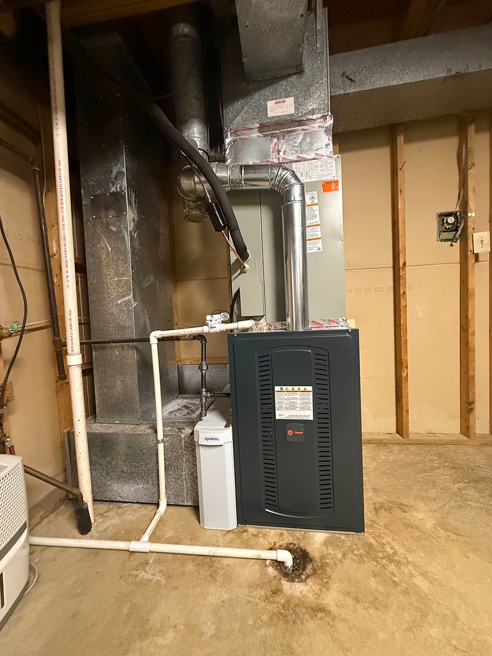 Furnace and water heater in a basement utility room with exposed pipes and unfinished walls