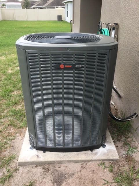 Outdoor central air conditioner unit beside a house on a concrete pad in a backyard.
