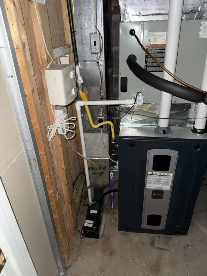 Furnace and water heater in a utility closet with exposed pipes and wiring.