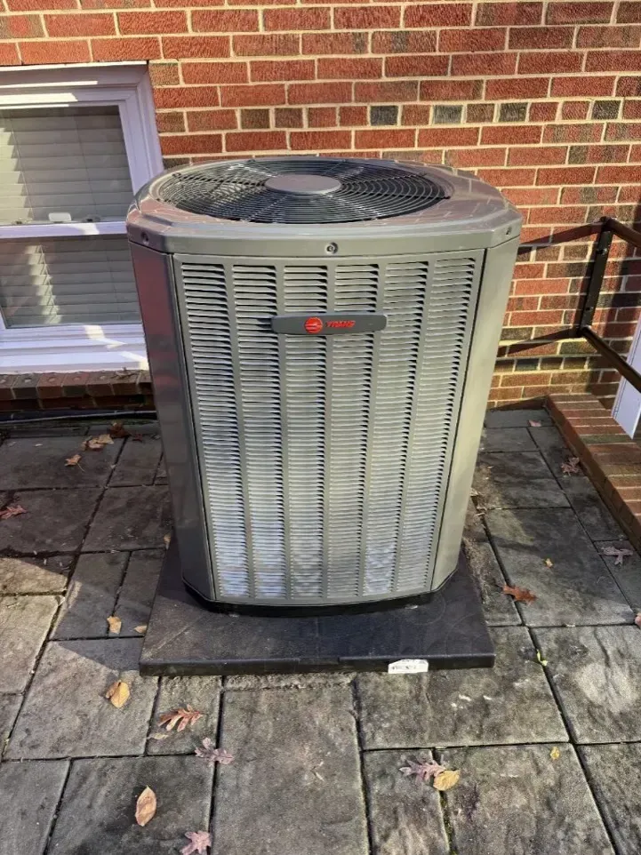 Outdoor air conditioning unit on a brick patio beside a brick wall and window