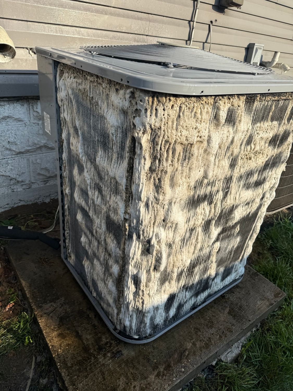 Dirty outdoor HVAC unit with mold and grime buildup on a concrete pad beside a house.