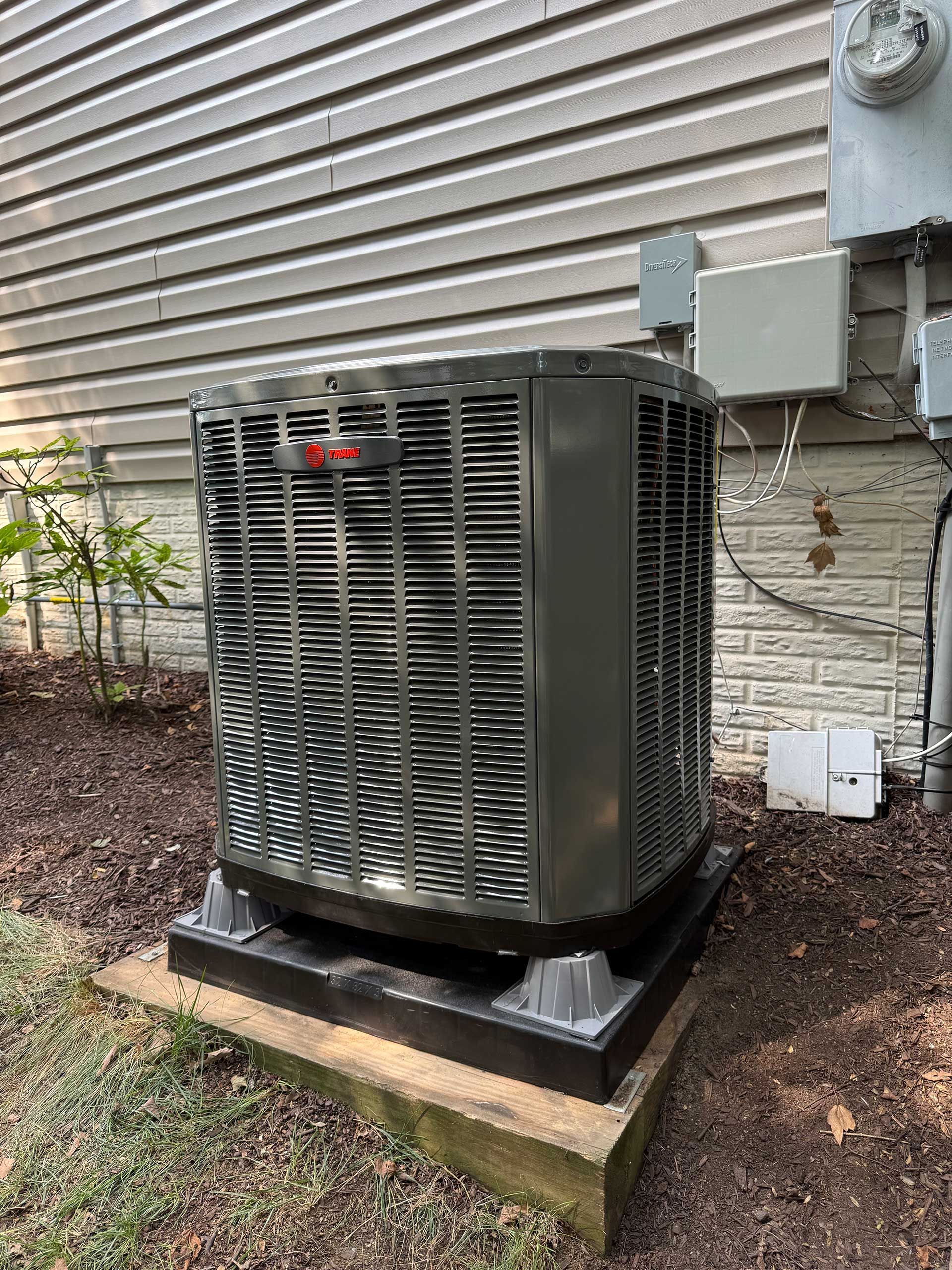 Outdoor HVAC unit with a dirty, dark mesh cover beside a building on a concrete pad