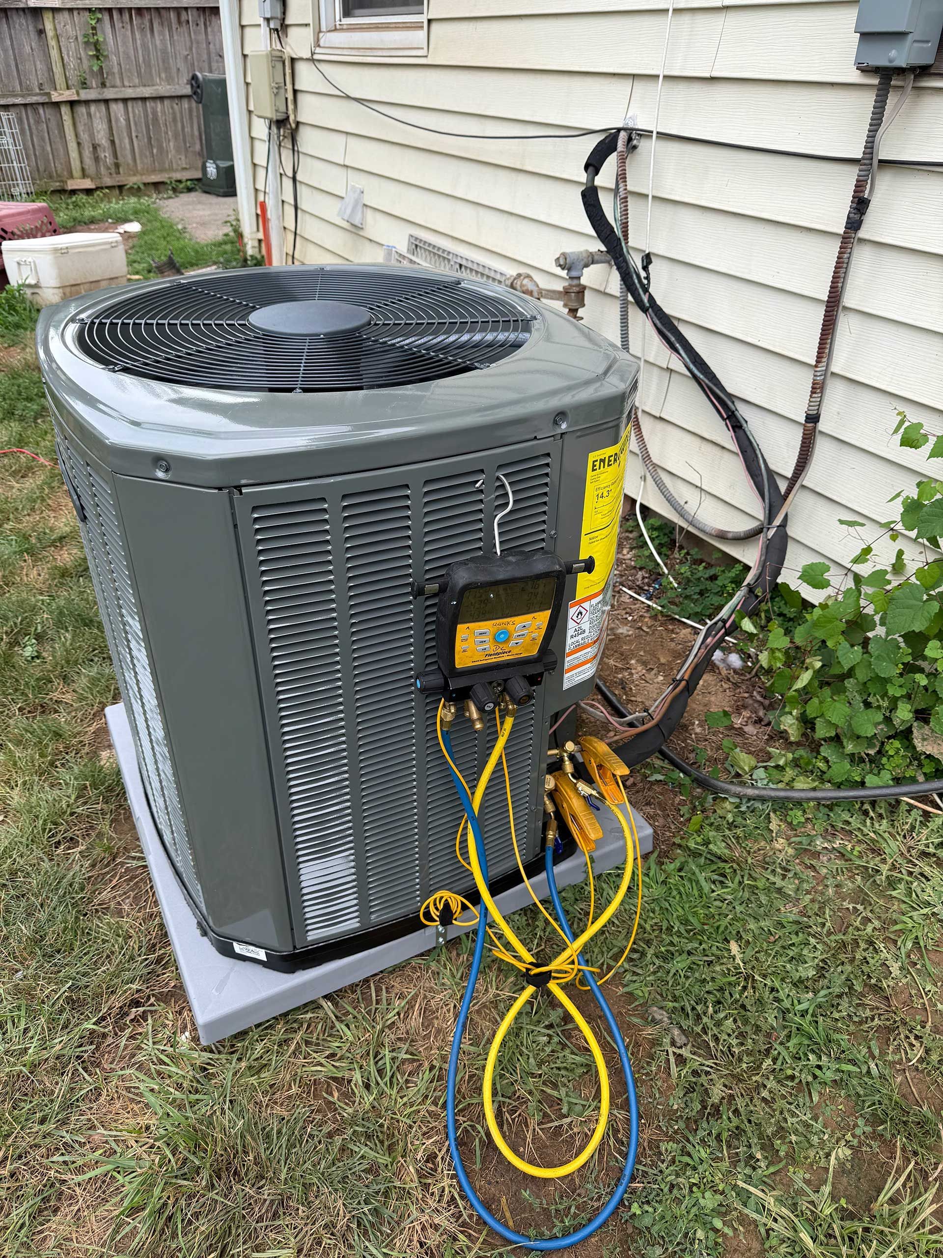 Outdoor air conditioner unit beside a house, with yellow and blue service gauges attached