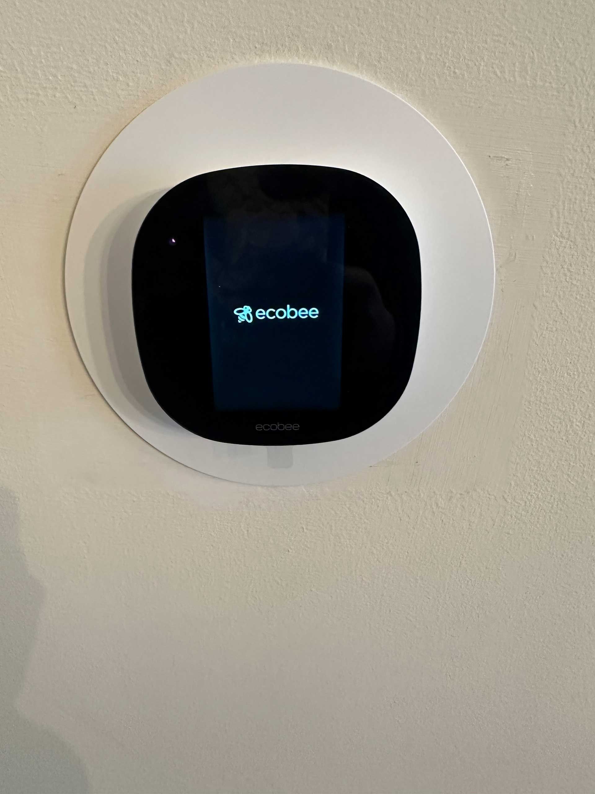 Wall-mounted thermostat with a black screen on a white ceiling or wall.