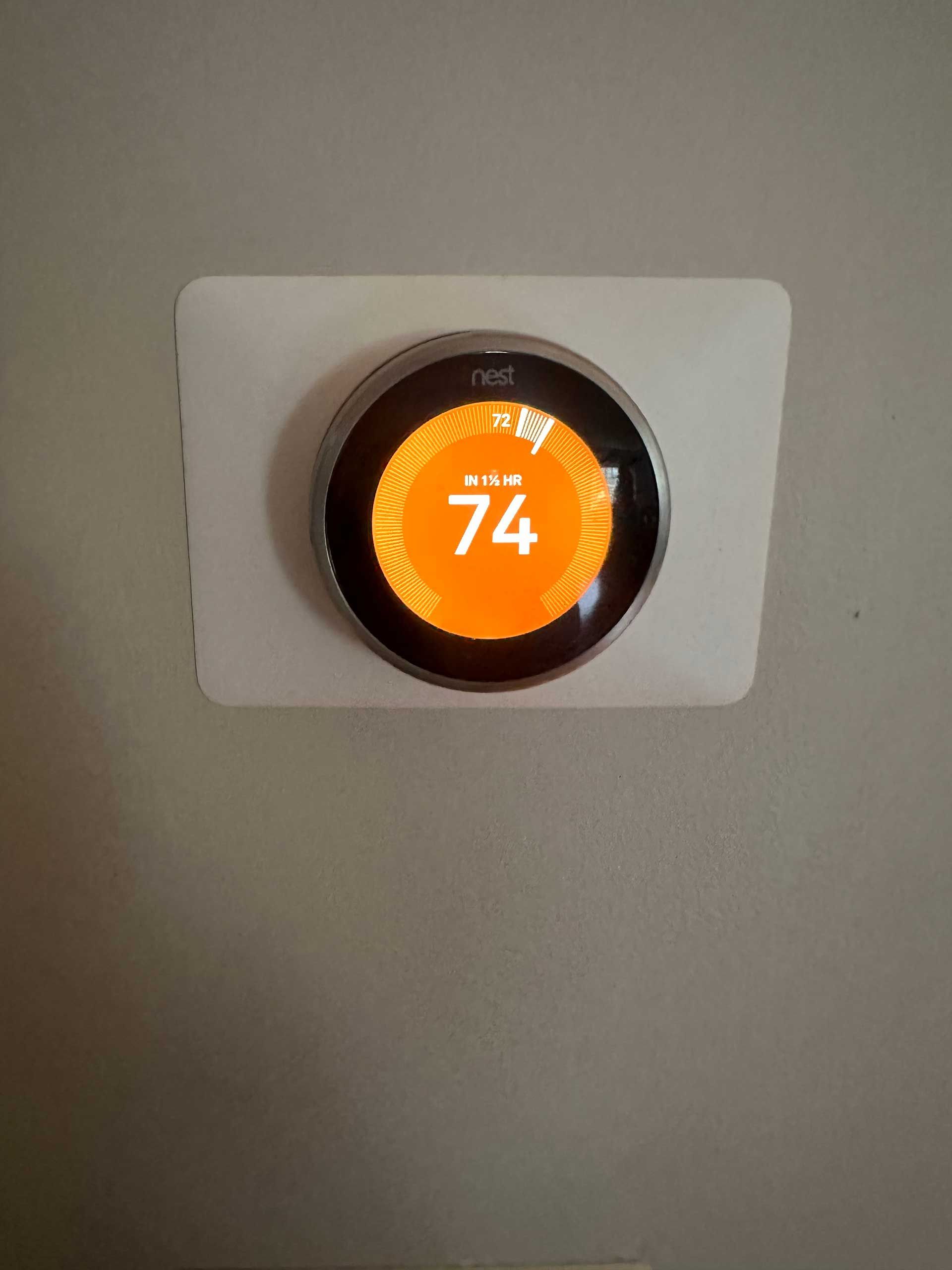 Orange thermostat display showing 74°F on a gray wall.