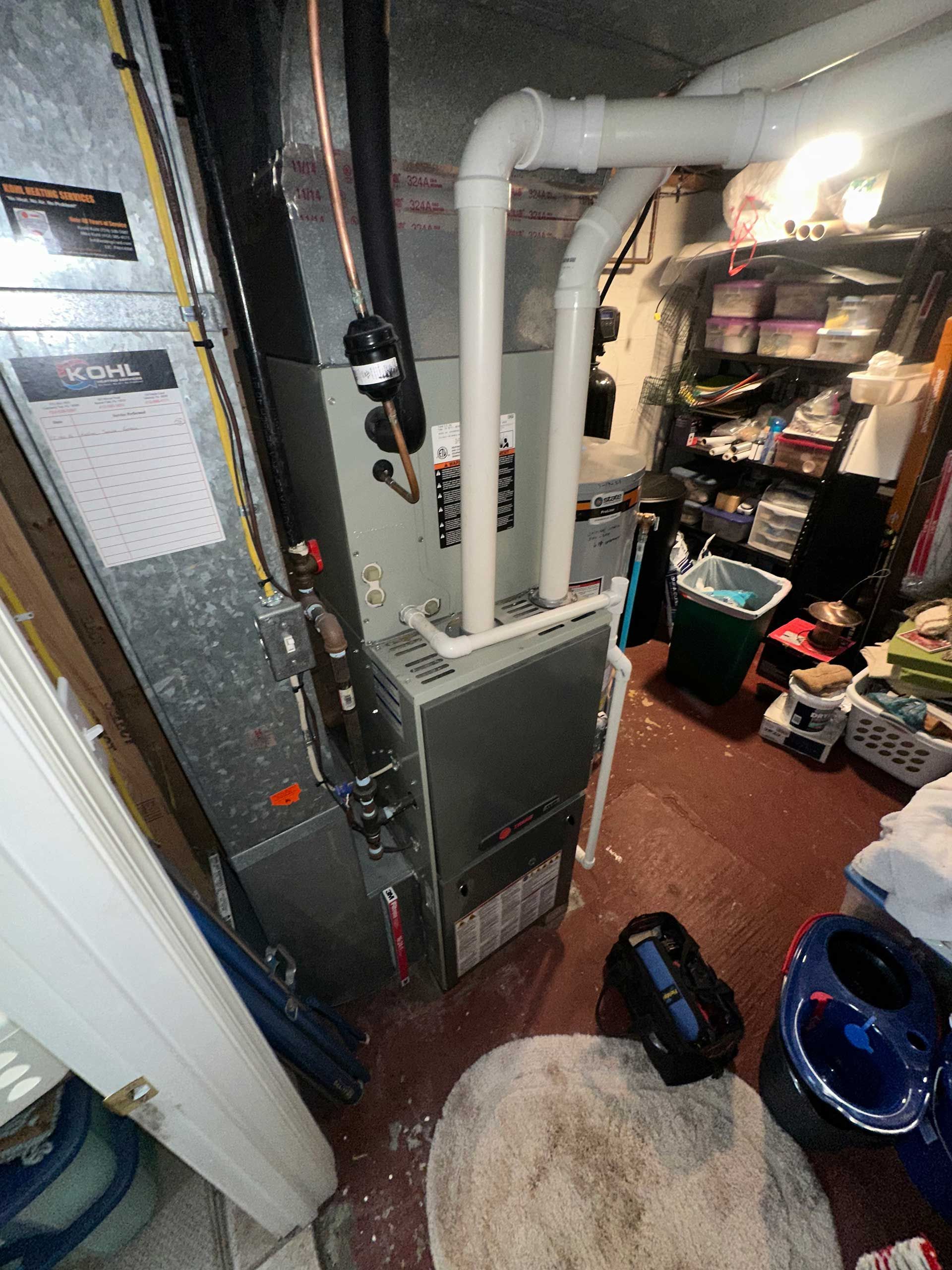 Basement furnace beside exposed ductwork and shelves, with tools and household items scattered on the floor