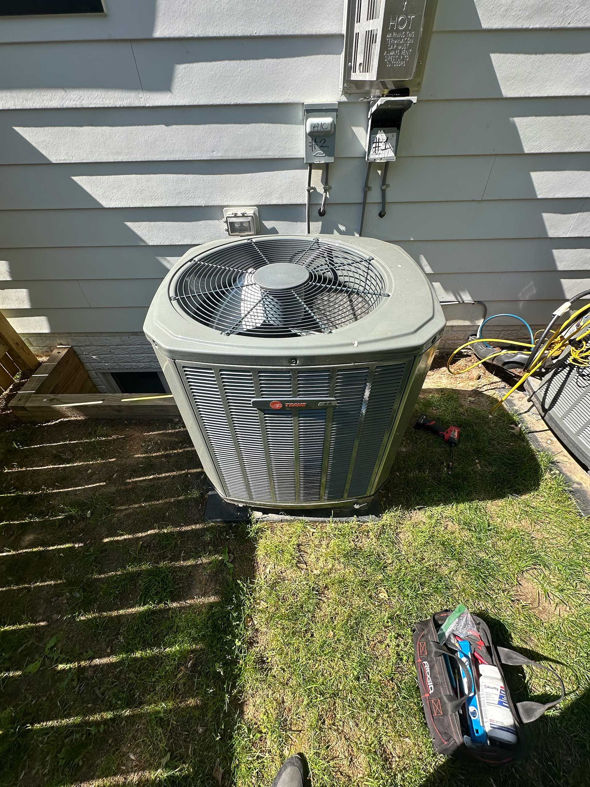 Outdoor air conditioner unit on grass beside a house wall with power cords nearby