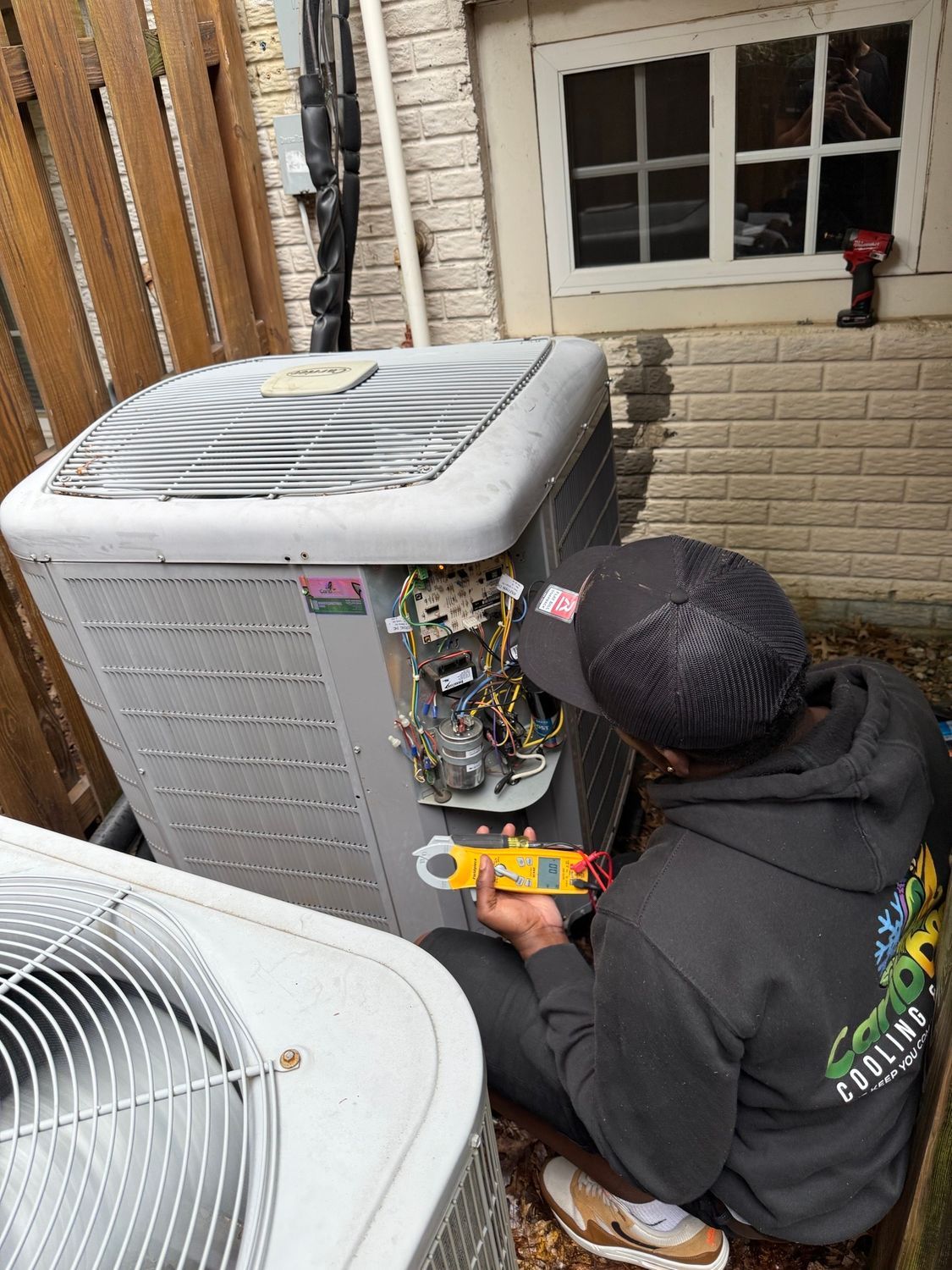 Technician inspecting outdoor HVAC unit with exposed wiring beside a house