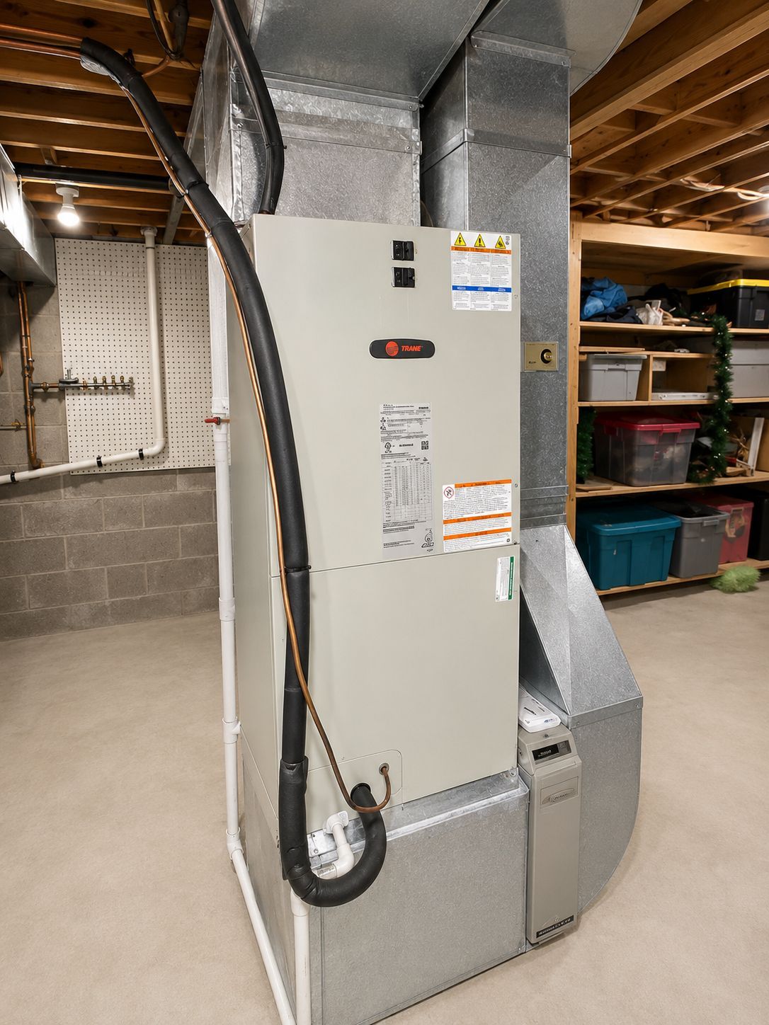 Gray furnace with attached ductwork and hose in a basement utility room.