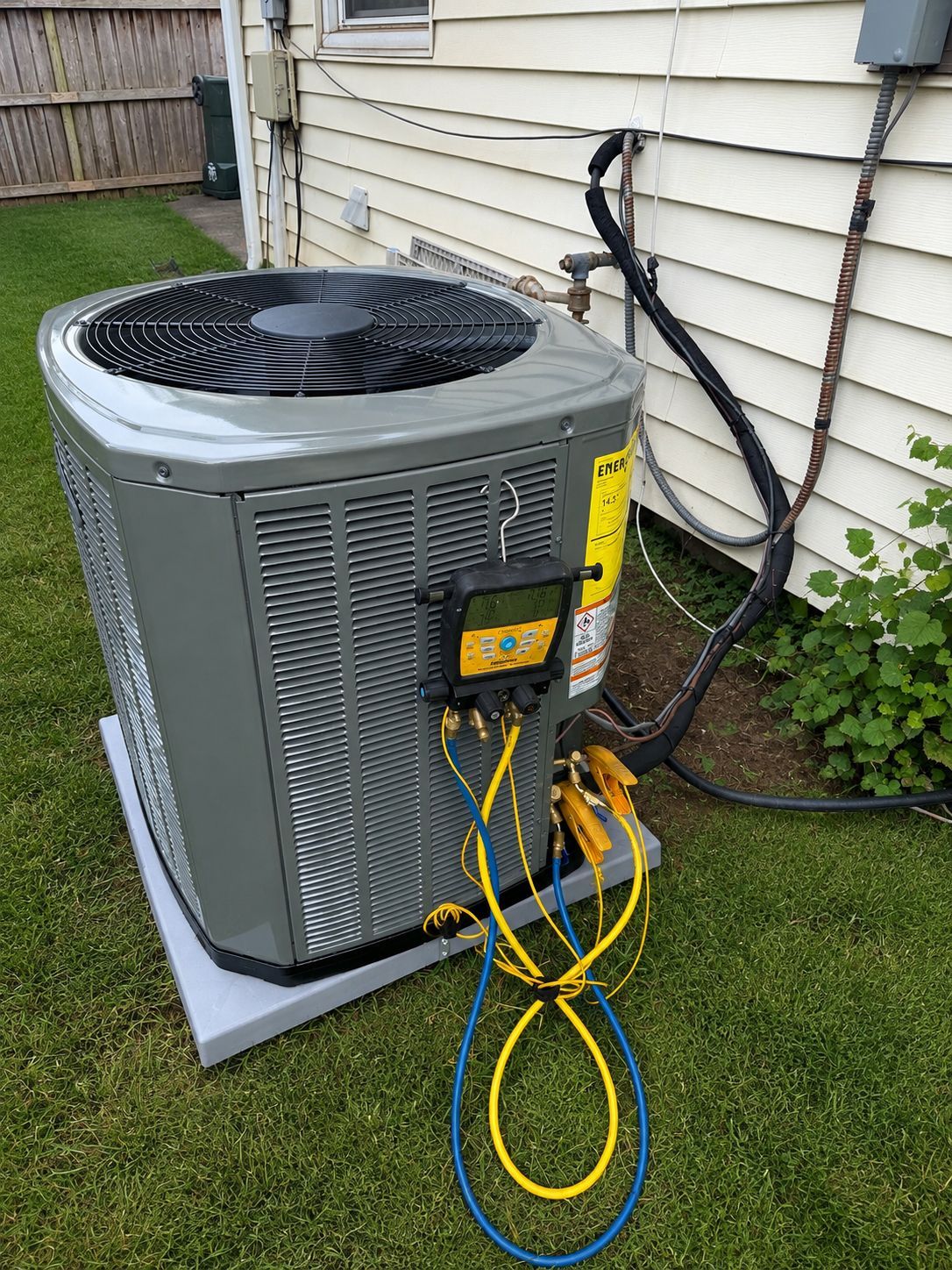 Outdoor HVAC condenser unit beside a house with yellow and blue service gauges attached